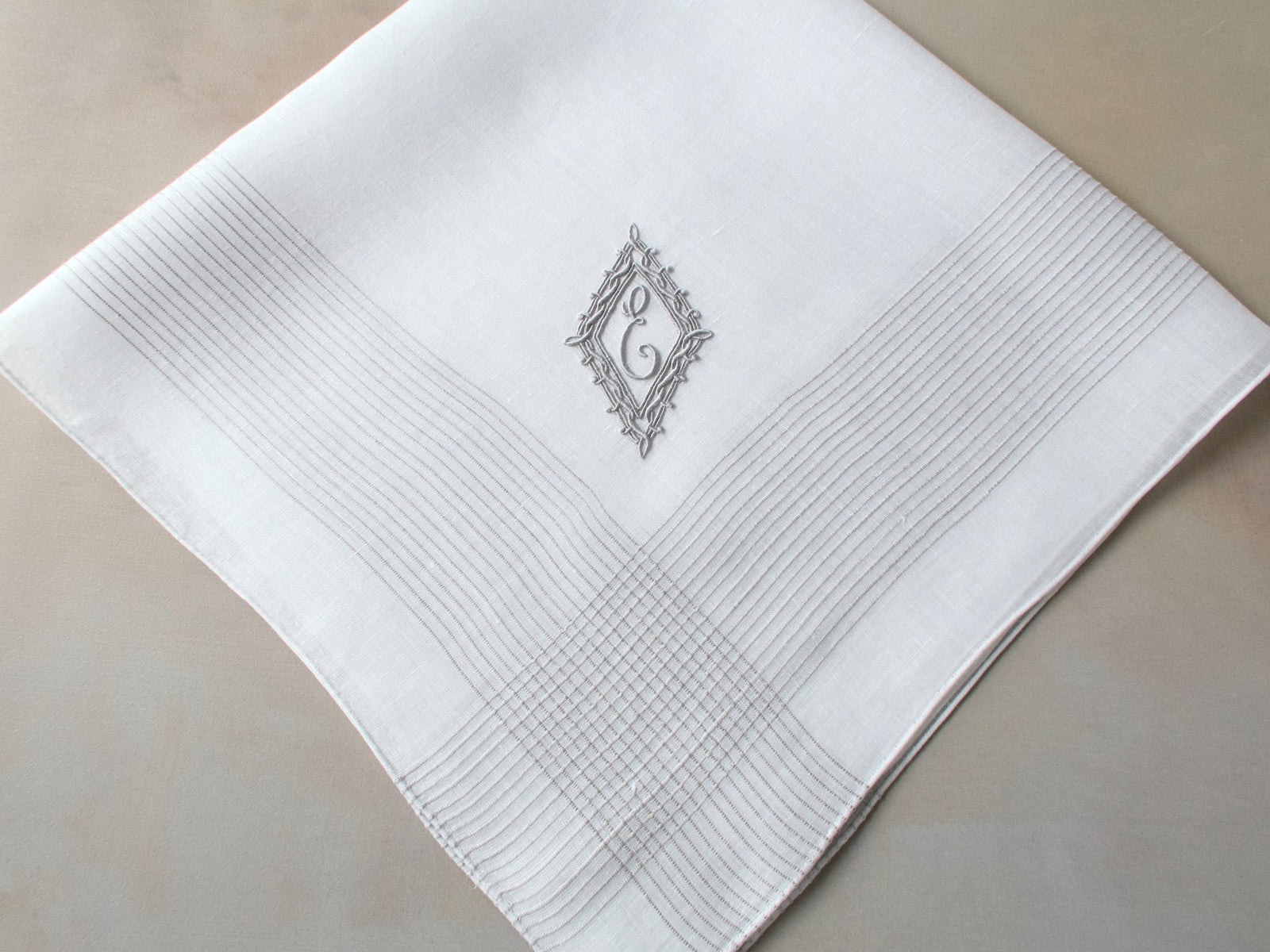 Vintage Marghab handkerchief featuring an “E” monogram framed in twisted cord and bordered by the “Hand Inserted Threads” pattern. Hand embroidered in Madeira on fine linen.