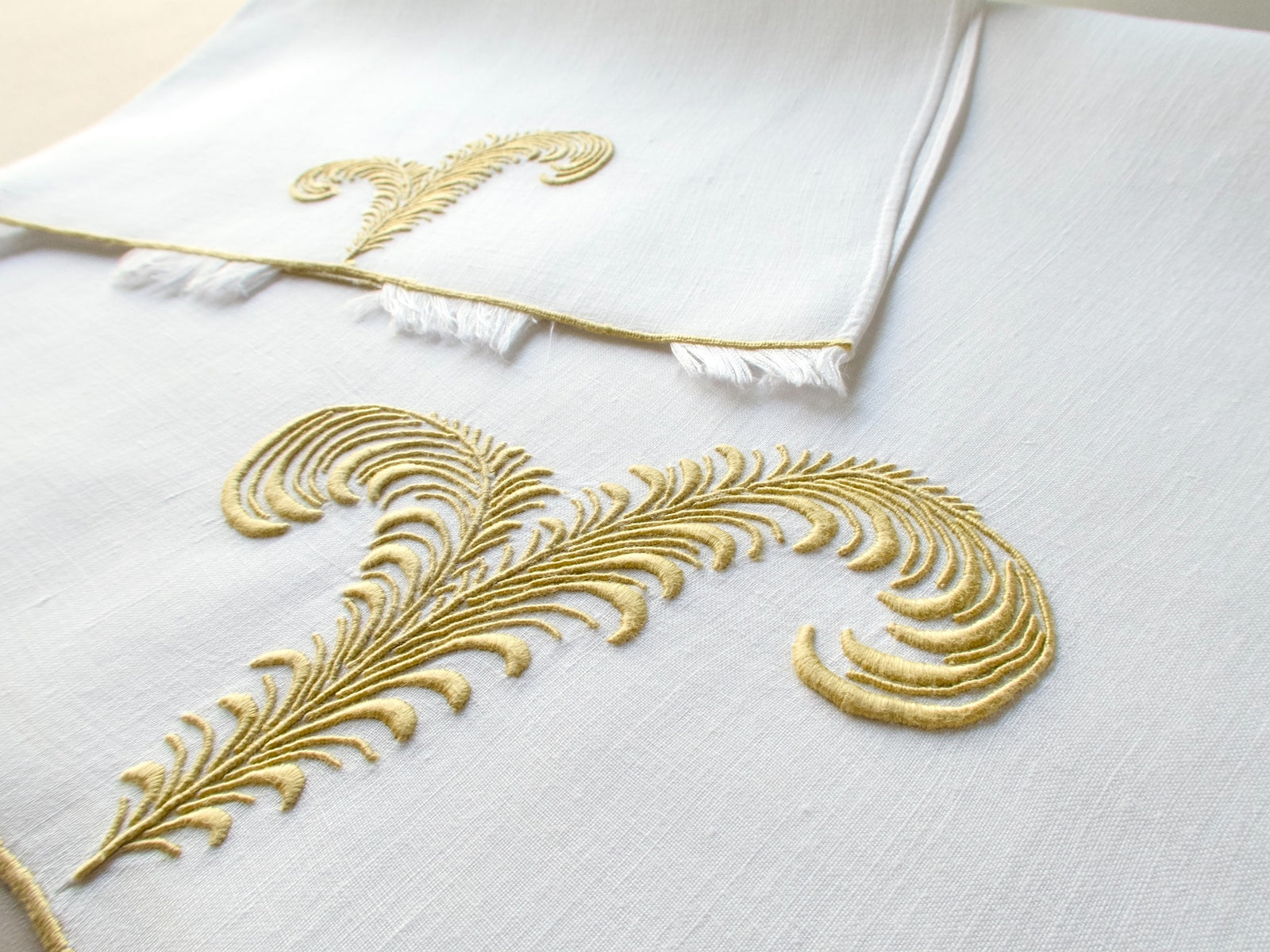 Marghab linen towels in the “Plume” pattern, hand embroidered in gold with feather motifs and eyelash fringe — fingertip and guest sizes shown.