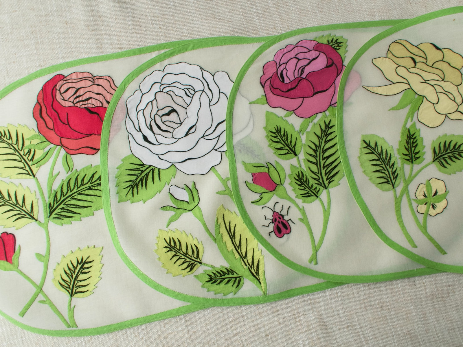 Four vintage Italian appliqué placemats with large-scale roses in red, white, pink, and yellow with ladybug detail on semi-sheer linen