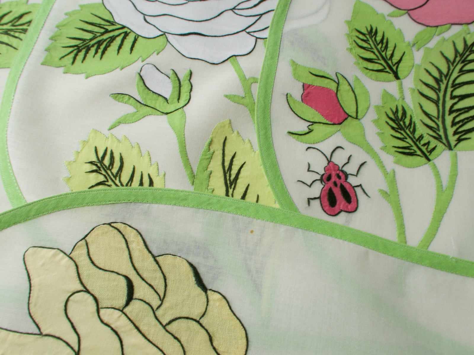 Close-up of vintage Italian appliqué placemat featuring big yellow rose and ladybug on semi-sheer linen with green border, showing small storage spot