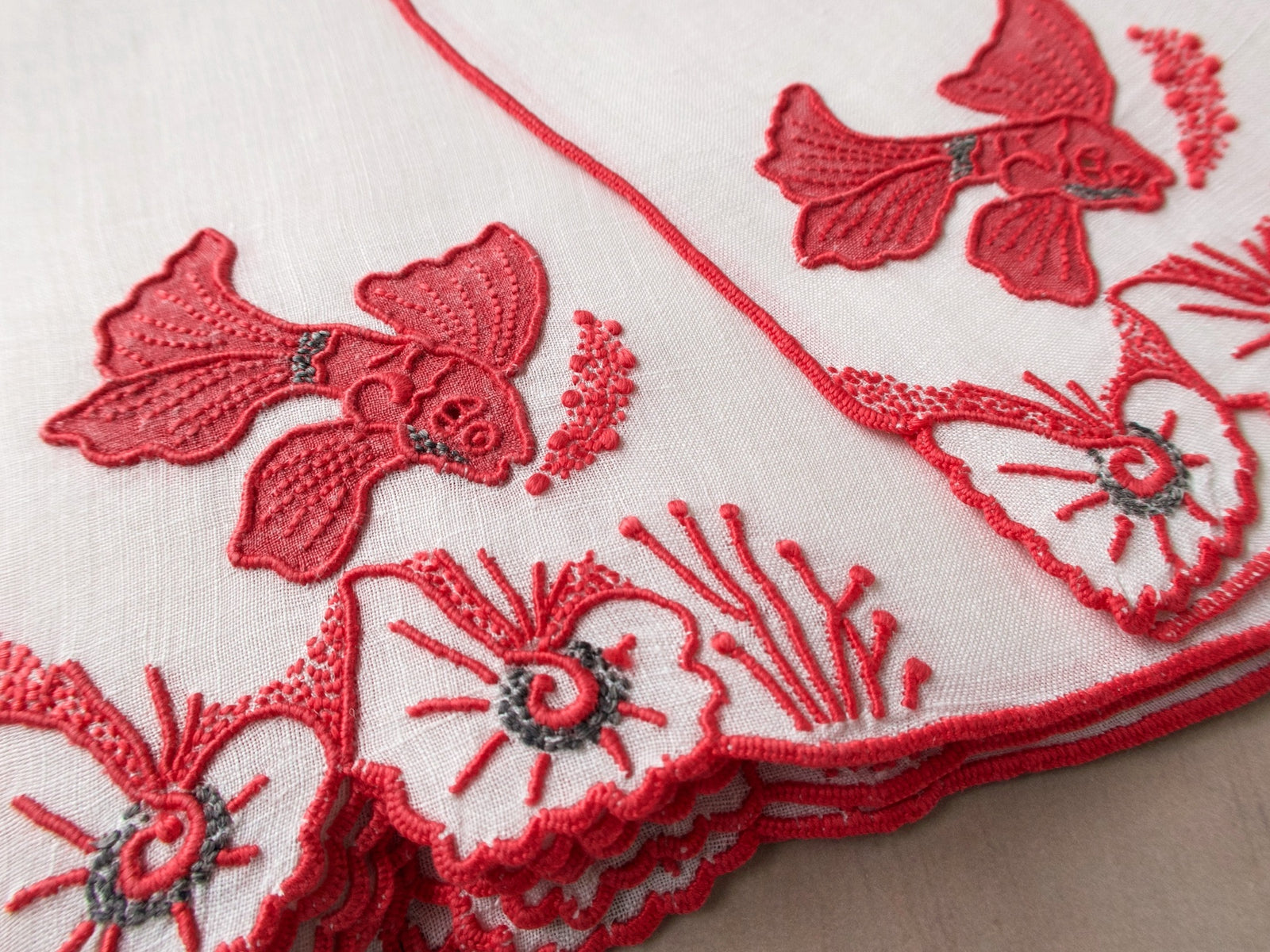 Close-up of vintage Marghab Tropical Fish cocktail napkin showing red appliqué and cutwork with gray accent stitching on white Irish linen