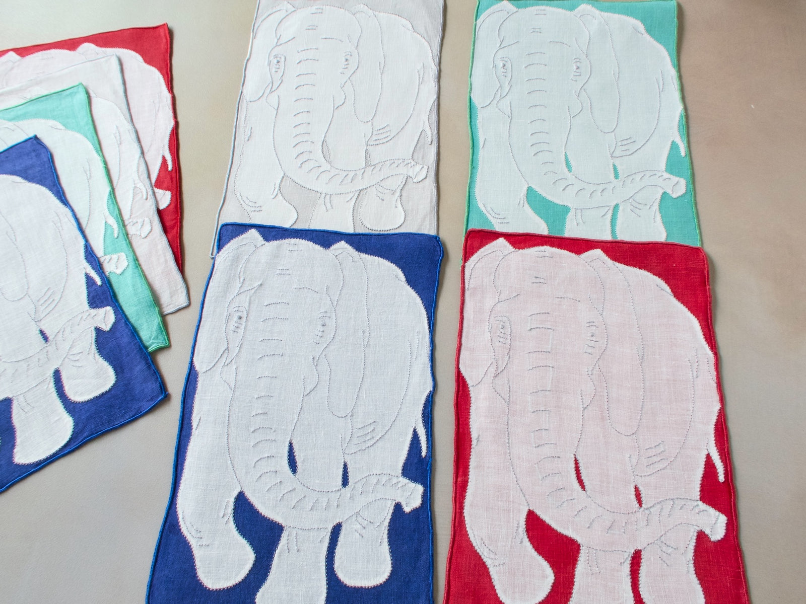 Full set of eight vintage Madeira elephant cocktail napkins showing all four background colors — red, teal, blue, and gray
