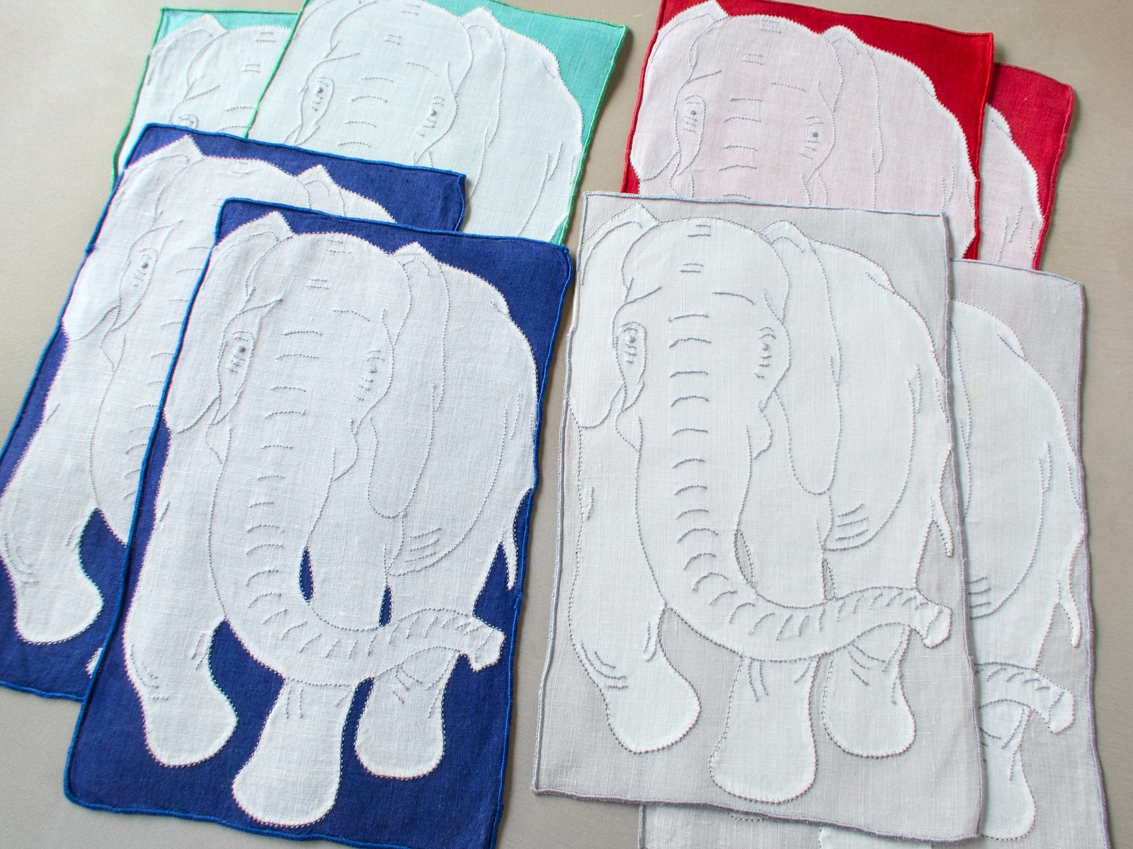Full set of eight vintage Madeira elephant cocktail napkins showing all four background colors — red, teal, blue, and gray