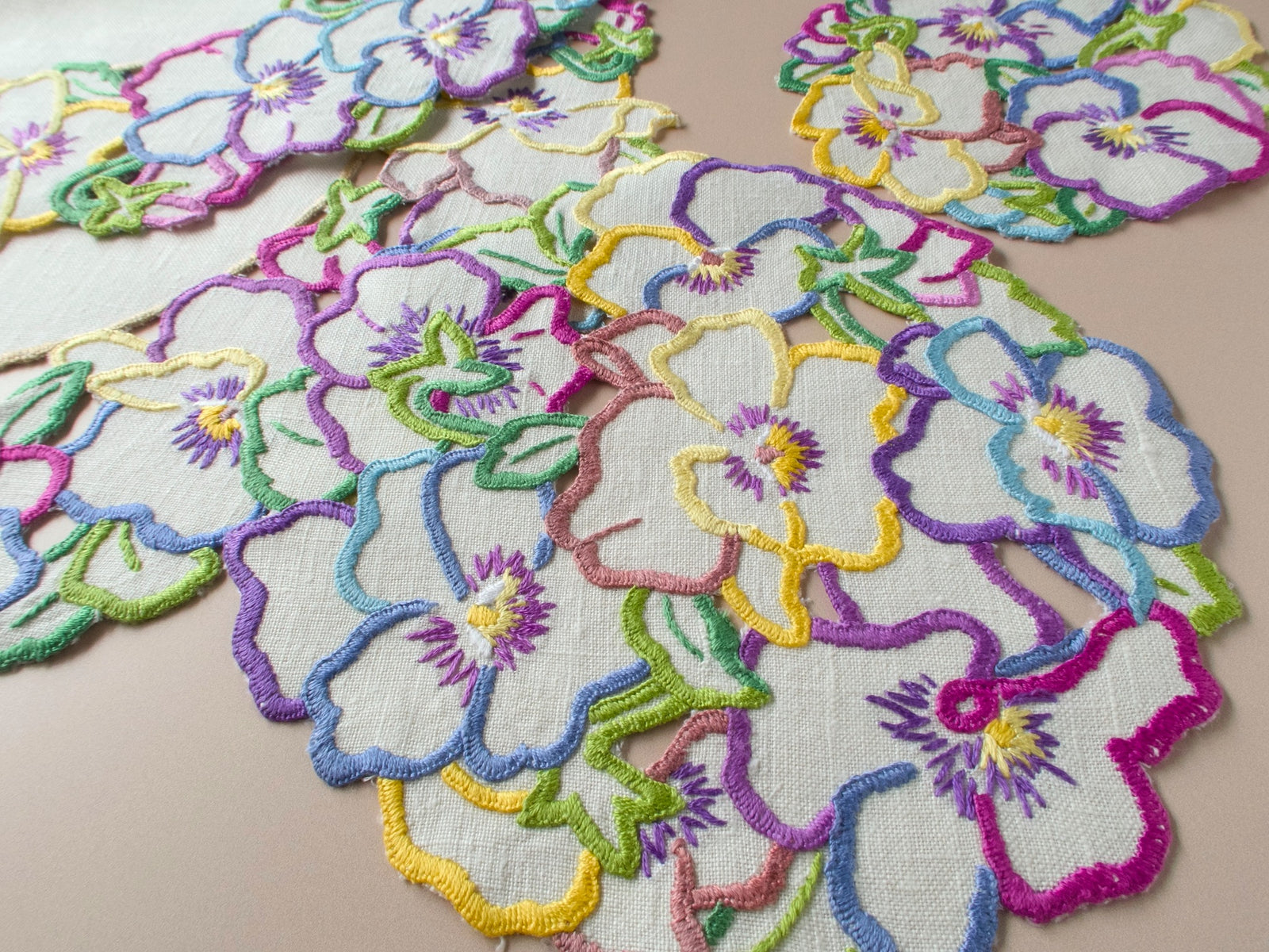 Close-up of vintage embroidered pansy centerpiece, multicolor satin stitch pansies in cheerful abundance on natural linen.