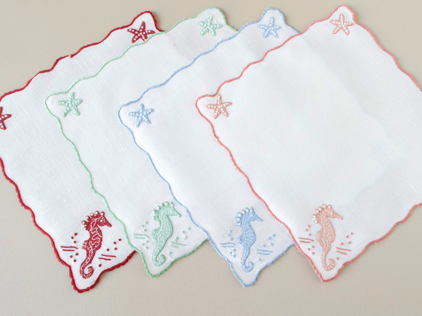 Close view of vintage Madeira seahorse cocktail napkins, showing appliqué and embroidery detail with scalloped edges.