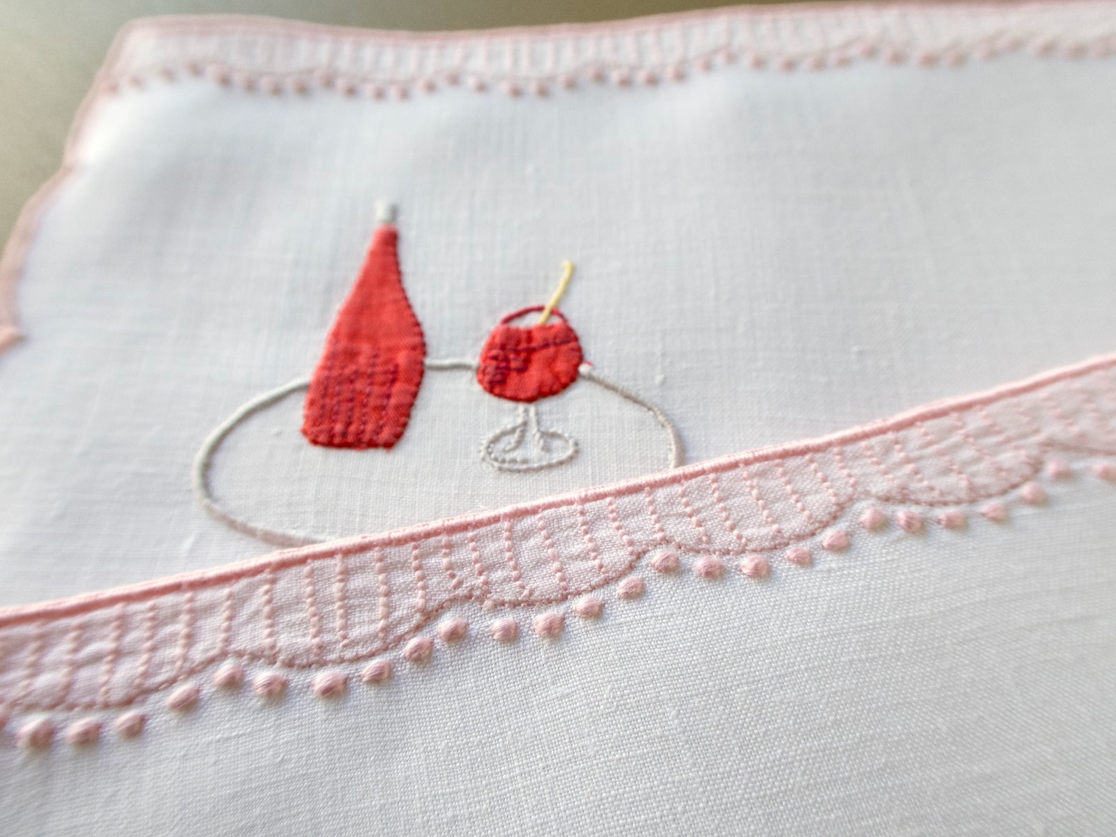 Pom-pom trim overhanging the hand embroidered café table scene on a vintage Madeira cocktail napkin