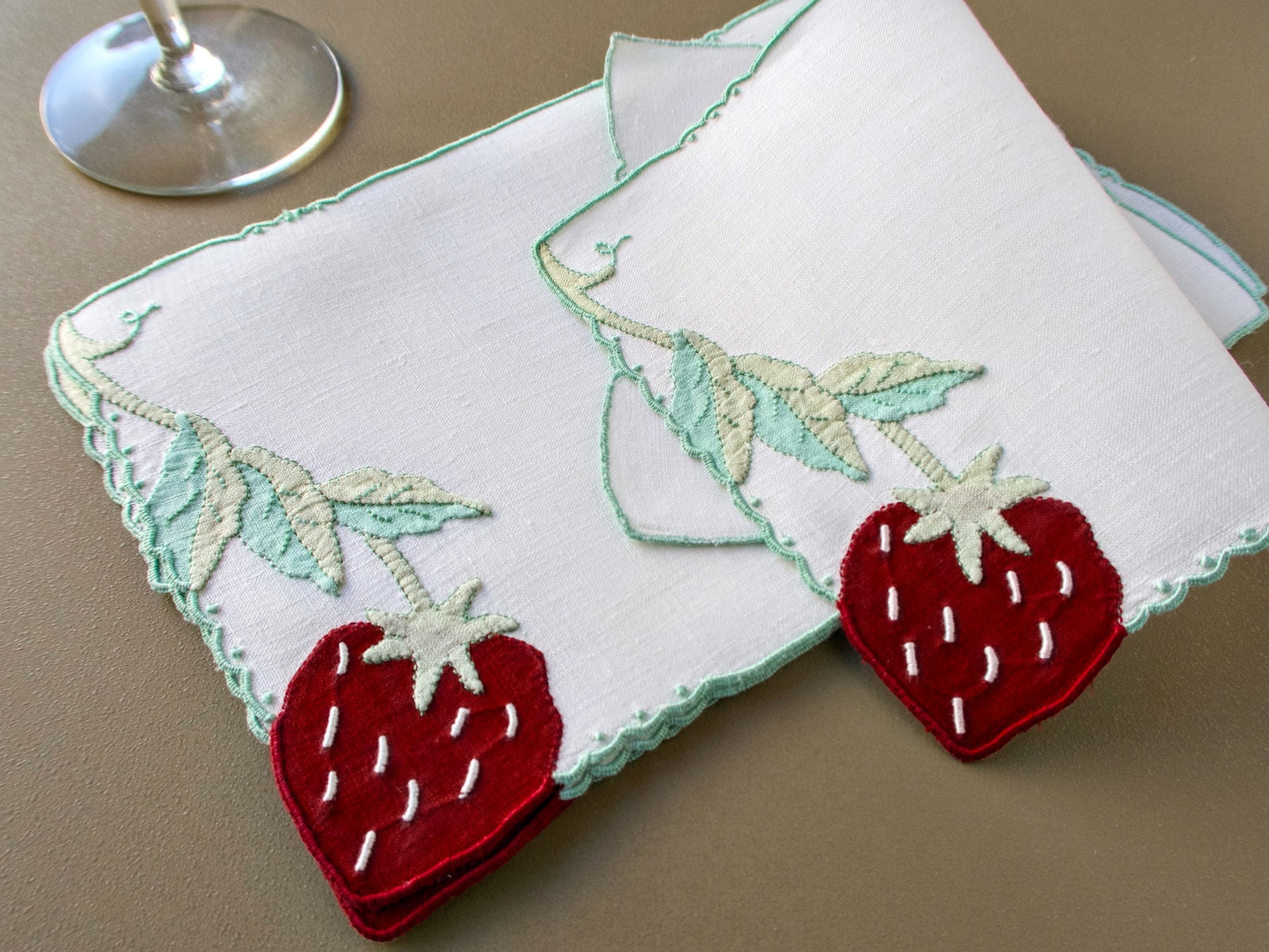 Two vintage Madeira cocktail napkins showing the strawberry and vine design beside a glass