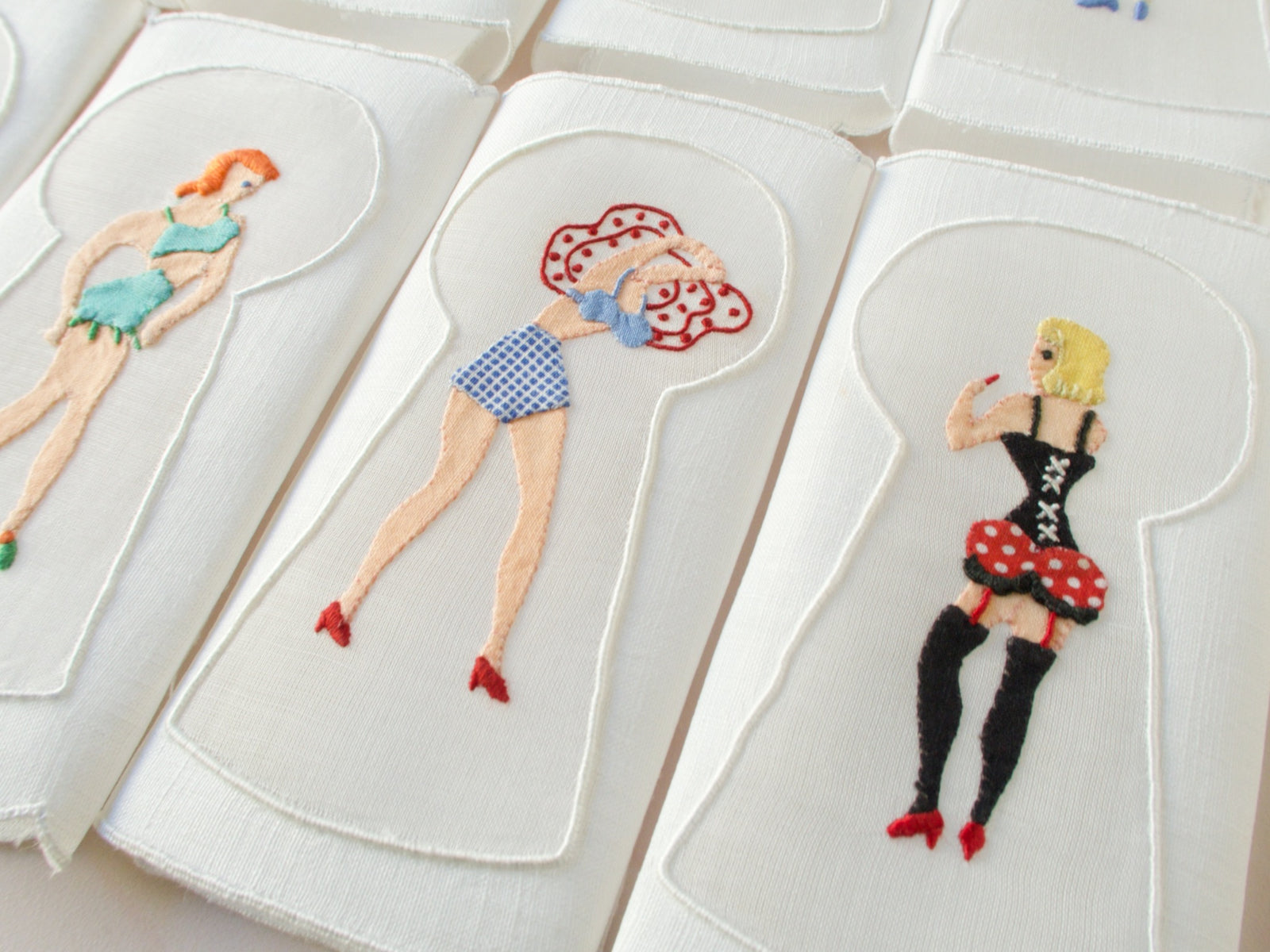 Hand-embroidered Madeira napkin with woman in red polka-dot skirt and black corset viewed through keyhole motif.