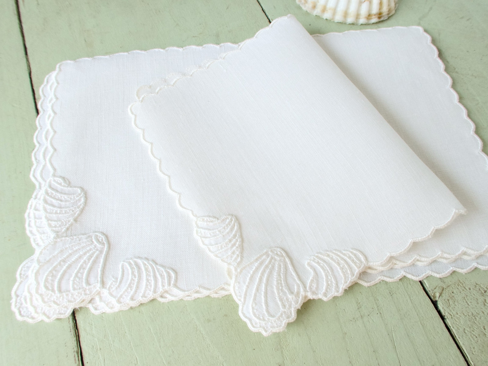 Vintage white Madeira embroidered cocktail napkins fanned and stacked, showing scalloped edges and shell motif.