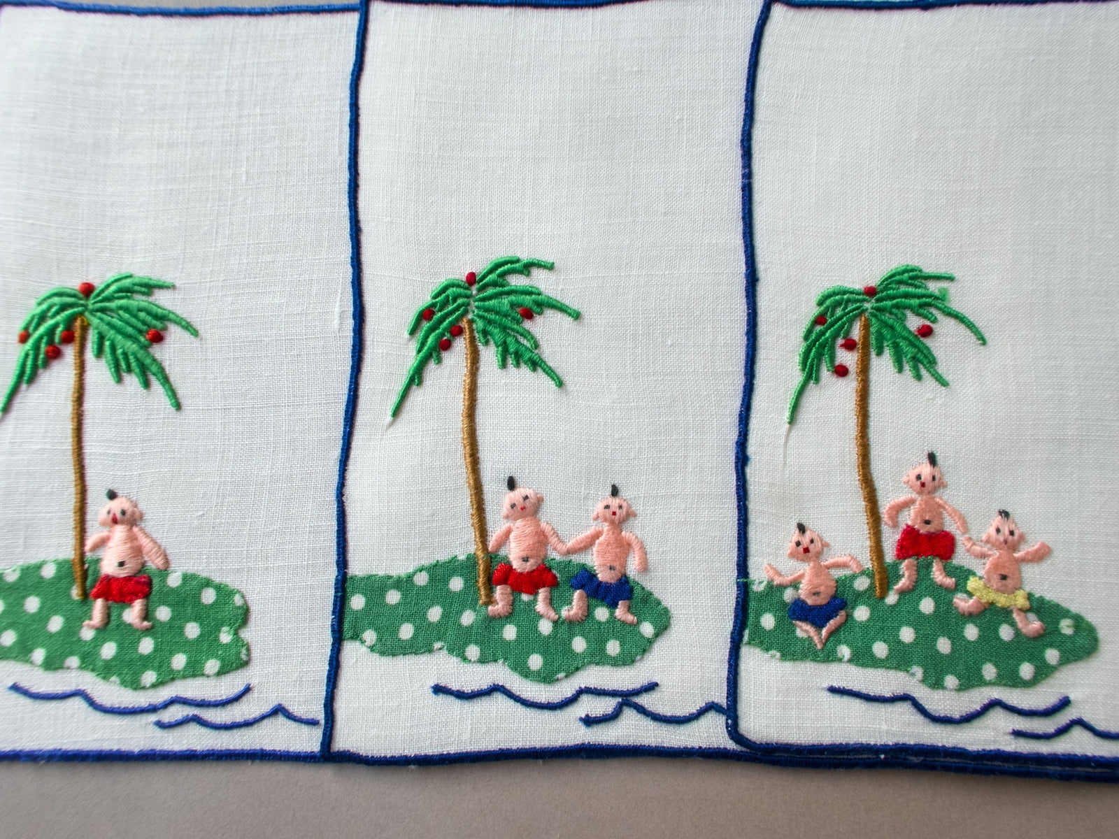 Vintage Madeira cocktail napkins showing playful embroidered scenes of babies on a tropical island beneath palm trees.