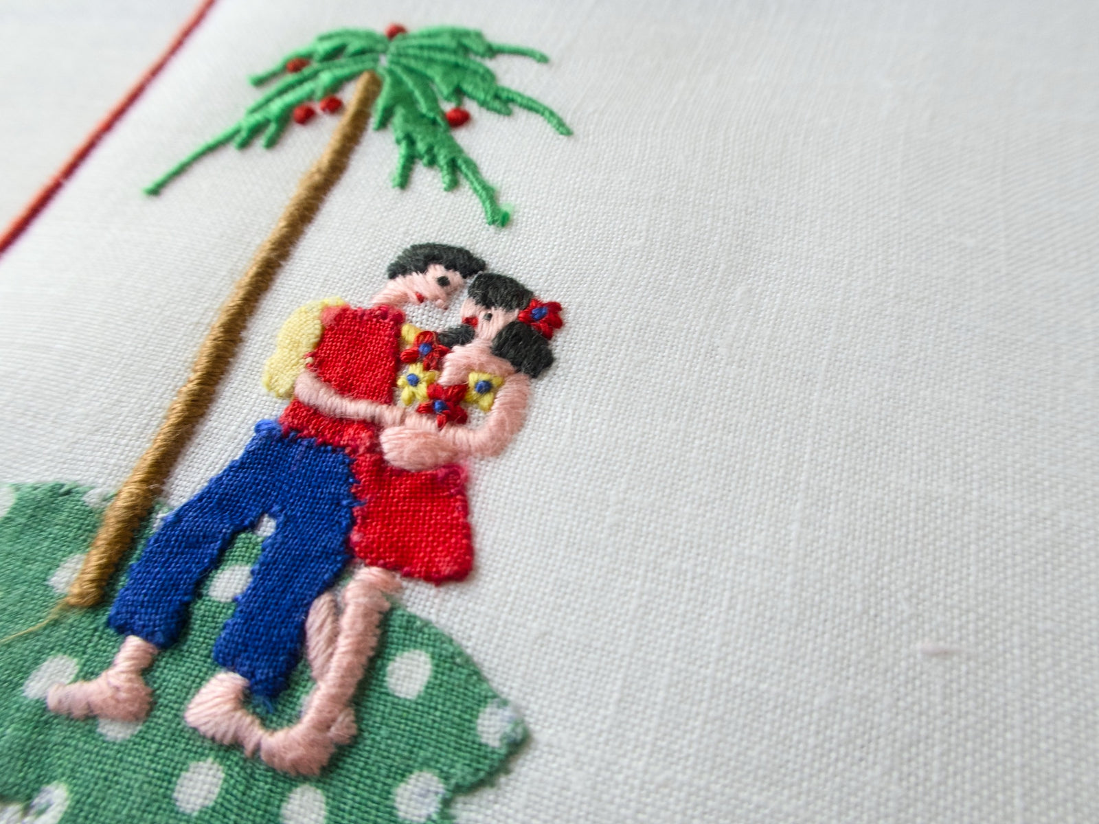 Man and woman embracing under a palm tree on vintage linen Madeira napkin.