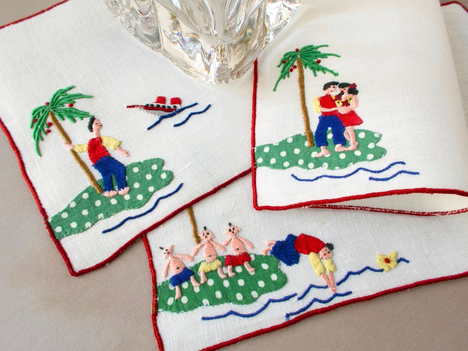 Vintage Madeira cocktail napkins showing playful tropical island scenes — a man stranded on an island, a couple embracing, and man swimming away from shore.