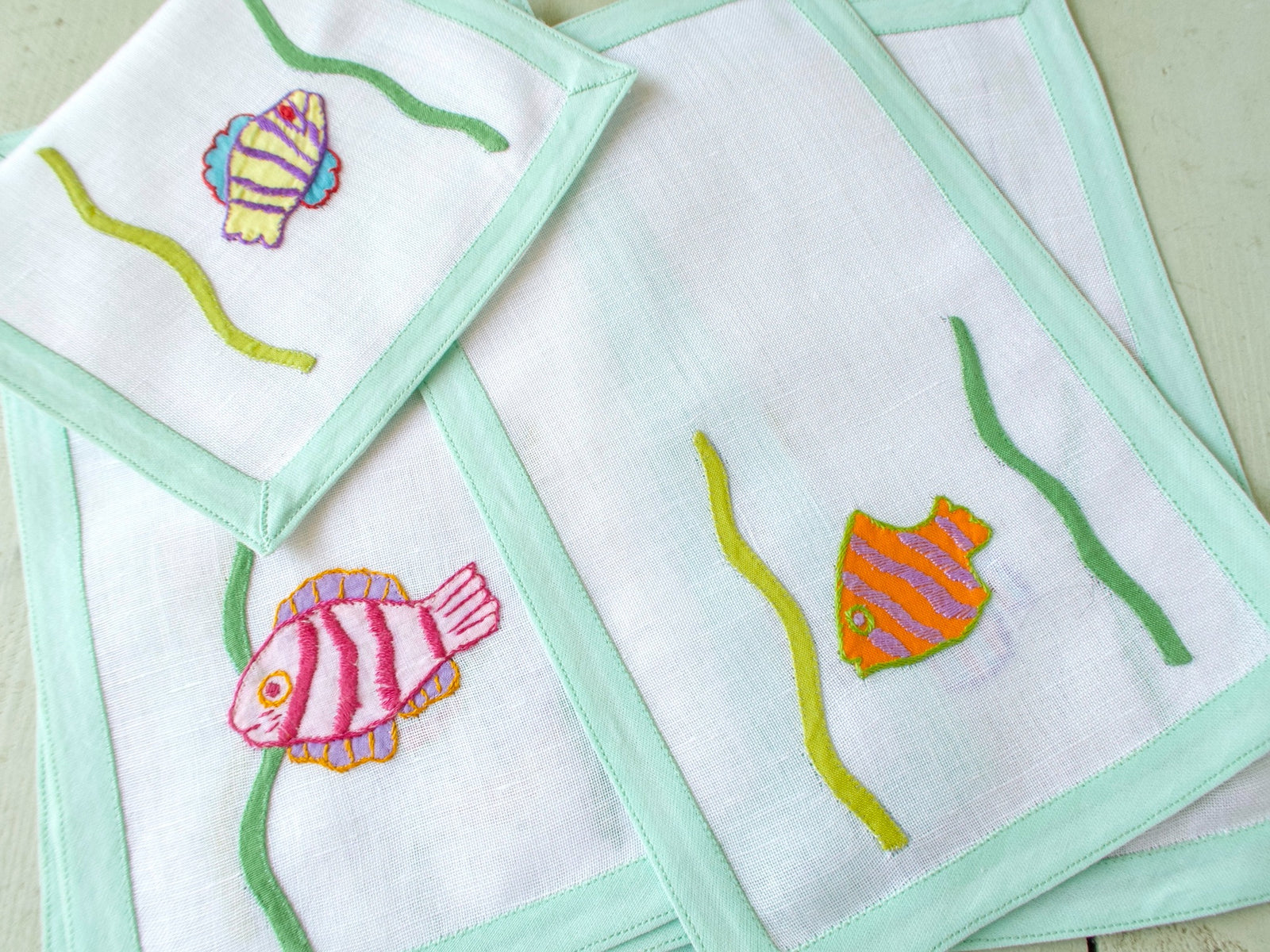 Close view of hand appliquéd tropical fish on vintage Léron semi-sheer linen cocktail napkin, celadon border detail.
