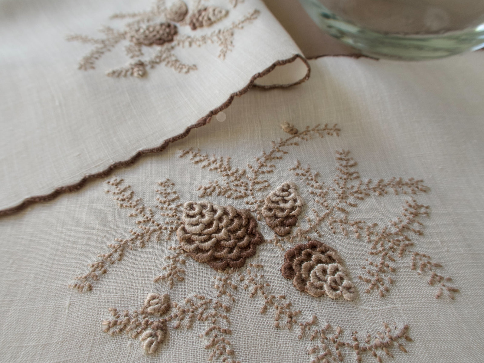 Close-up of embroidered pinecone motif on a vintage Marghab cocktail napkin in the “Pine Cones” pattern on fine linen, hand embroidered in Madeira with raised pinecone motifs and a scalloped edge.