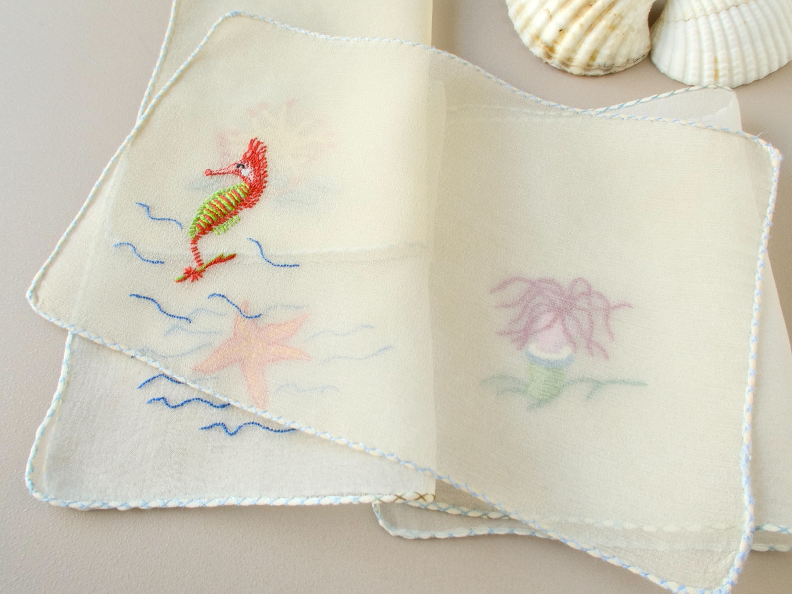 Vintage French silk chiffon cocktail napkins fanned and gathered, showing embroidered sea life motifs and semi-sheer ground.