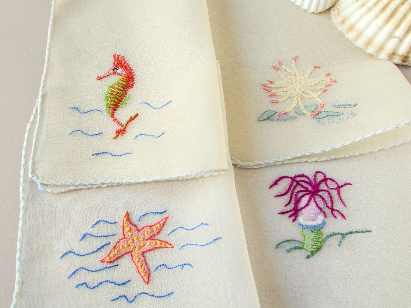 Close view of hand embroidered seahorse and starfish on vintage French semi-sheer silk chiffon cocktail napkin, delicate color detail.