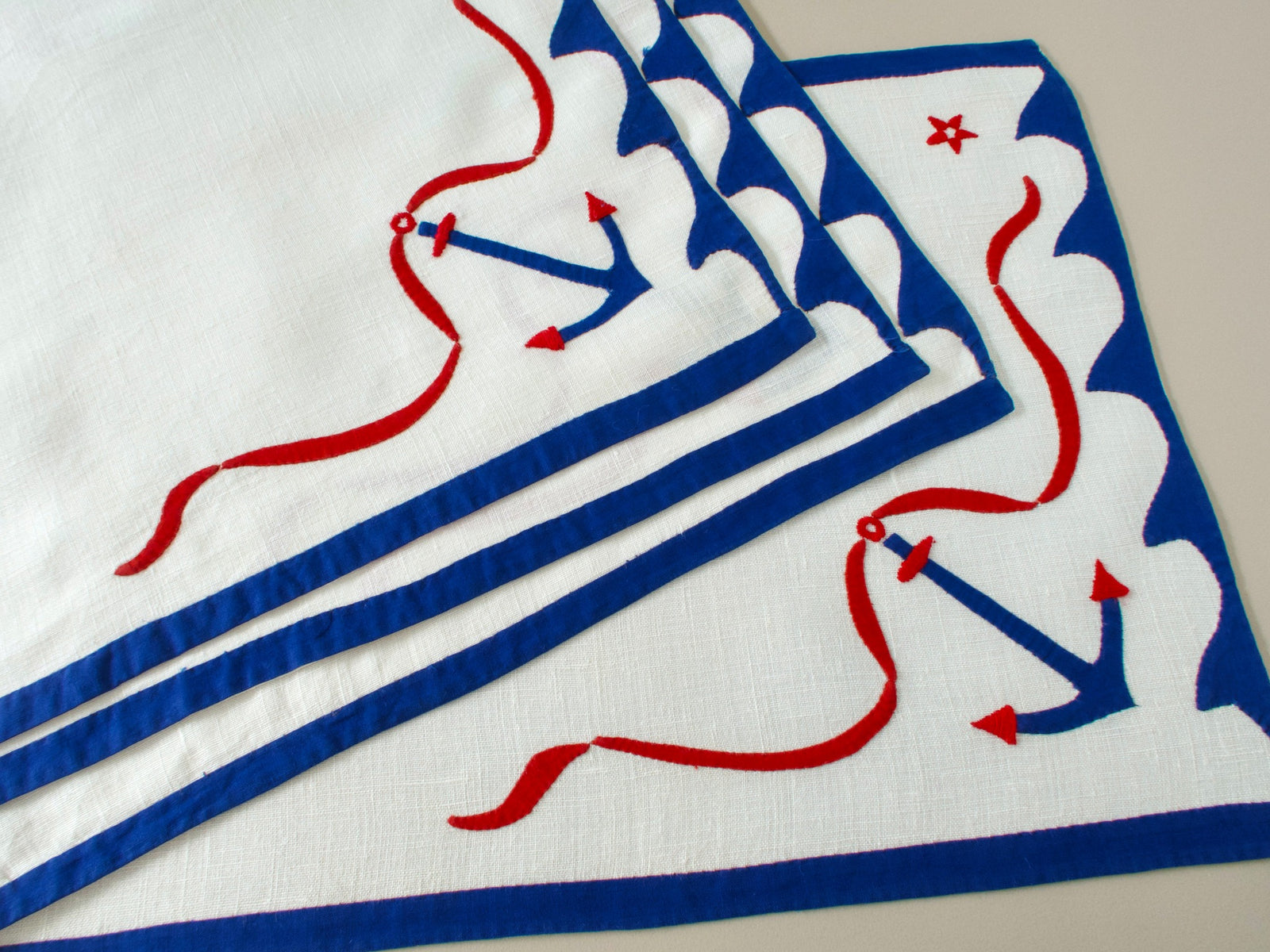 Vintage nautical linen placemats stacked and fanned, showing blue anchor, red stars and scalloped blue border design.