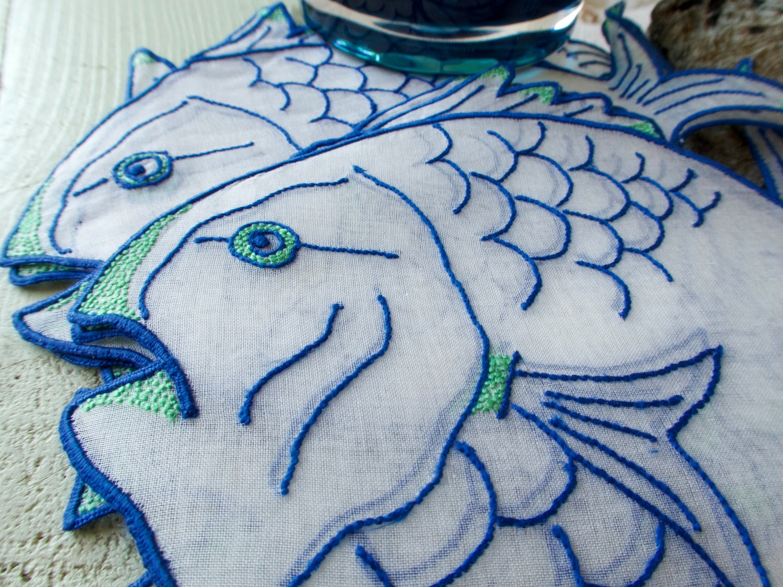 A set of vintage organdy cocktail napkins featuring hand embroidery of bold tropical fish in blue and green on a white background.