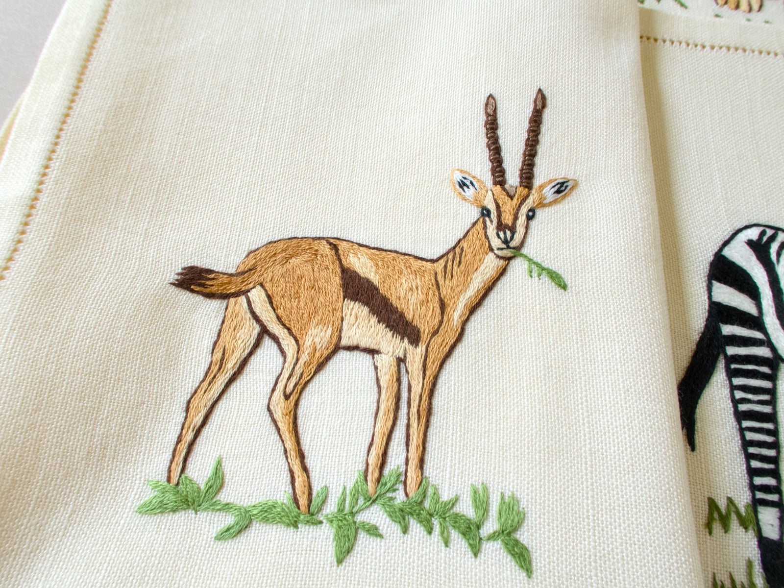 Close-up of vintage hand embroidered placemat showing gazelle standing in grass, detailed naturalistic embroidery on linen