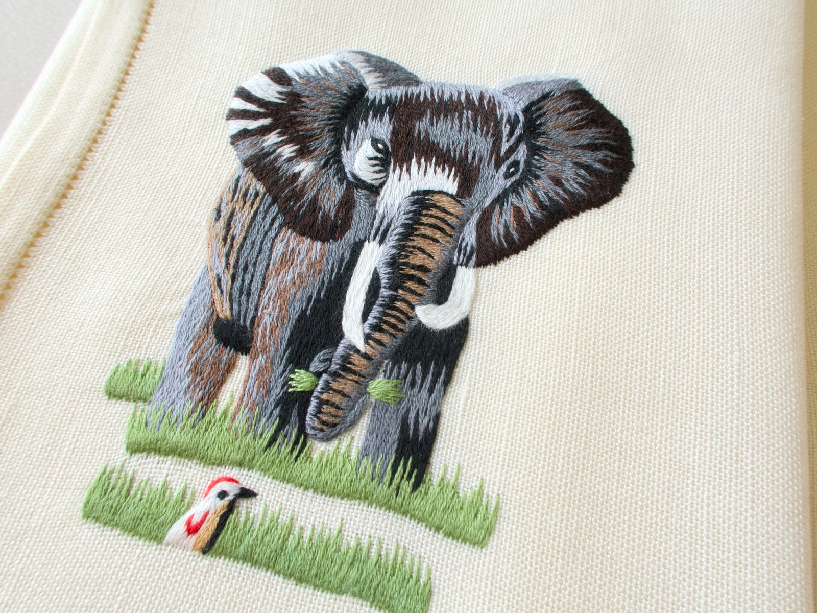 Close-up of vintage hand embroidered placemat showing elephant with detailed naturalistic embroidery on linen