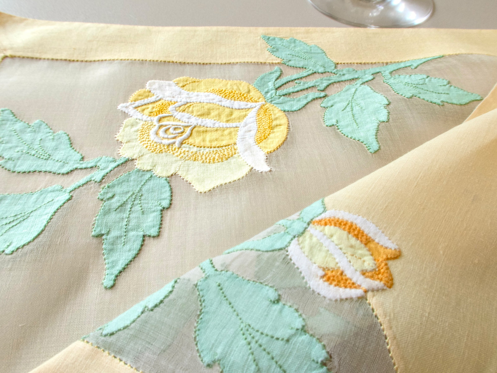 Close-up of vintage Madeira organdy placemat showing large yellow rose in full bloom with sage green linen leaf appliqué