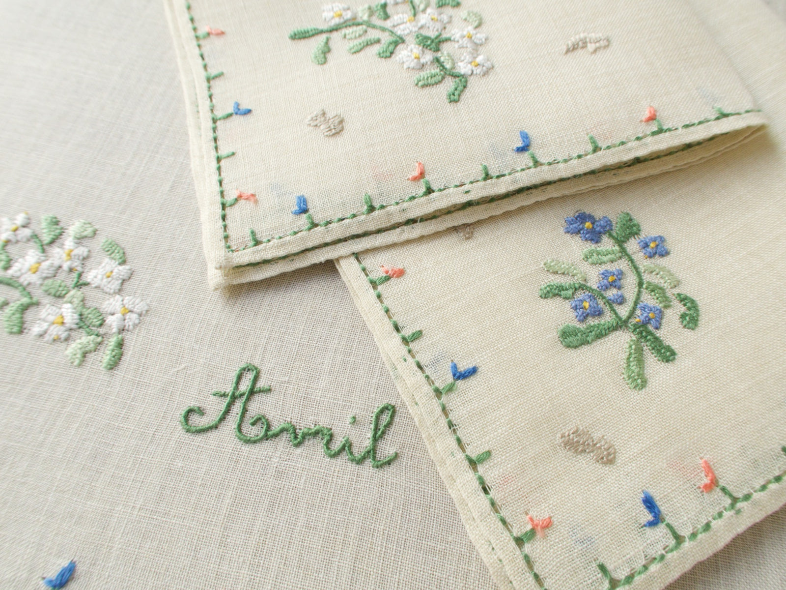 Folded linens showing Rapisardi’s April motifs: floral borders, decorative stitching.