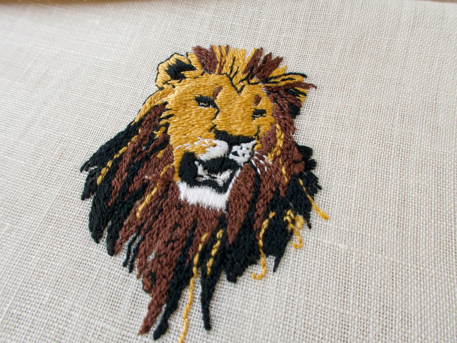 Single vintage cocktail napkin showing detailed lion head embroidery, semi-sheer ecru linen with brown border