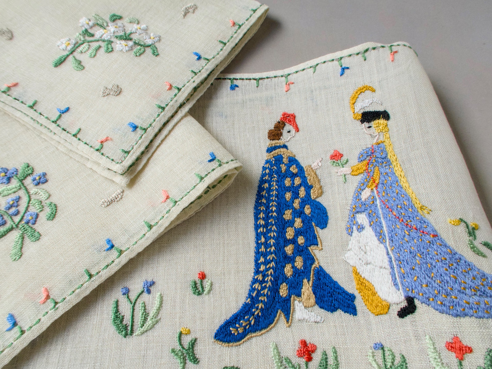 Medieval couple exchanging rings, embroidered on light linen with blue, gold and lavender garments and small floral details.