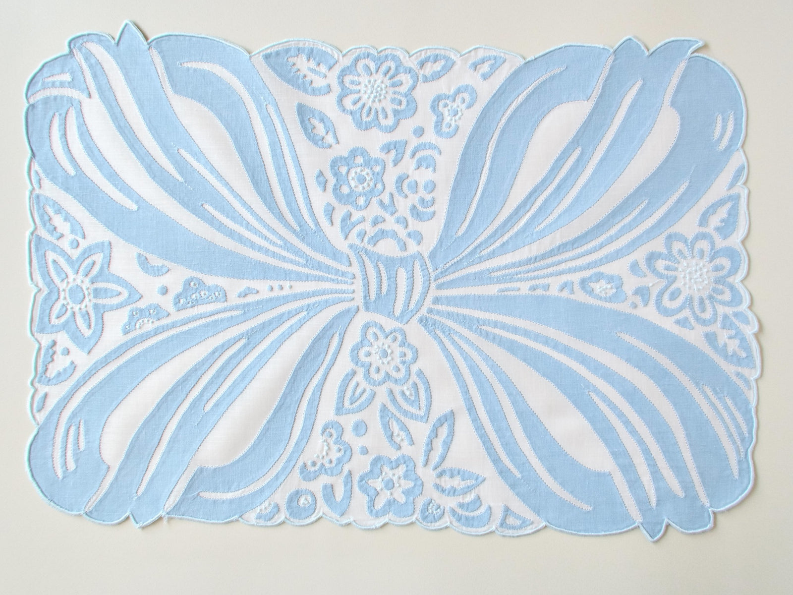 Top down view of a vintage Madeira hand embroidered placemat in bow design.