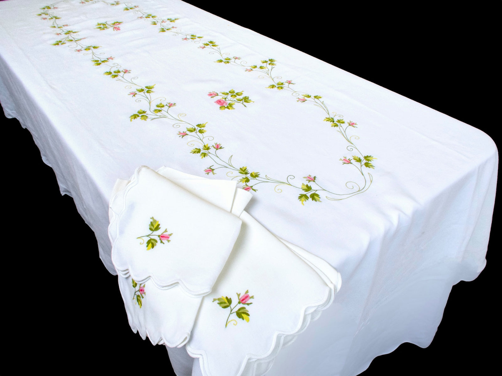 Full view of D. Porthault oval tablecloth on rectangular table with scalloped napkins showing rosebud embroidery
