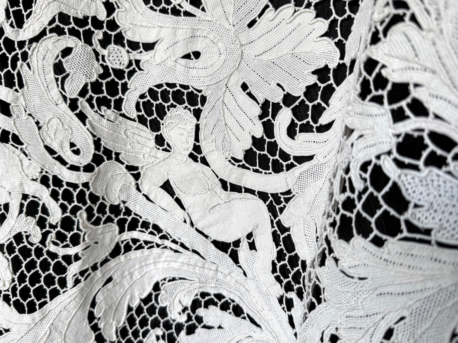 Reclining figure worked into the creamy white lace among sweeping leaves and open mesh.
