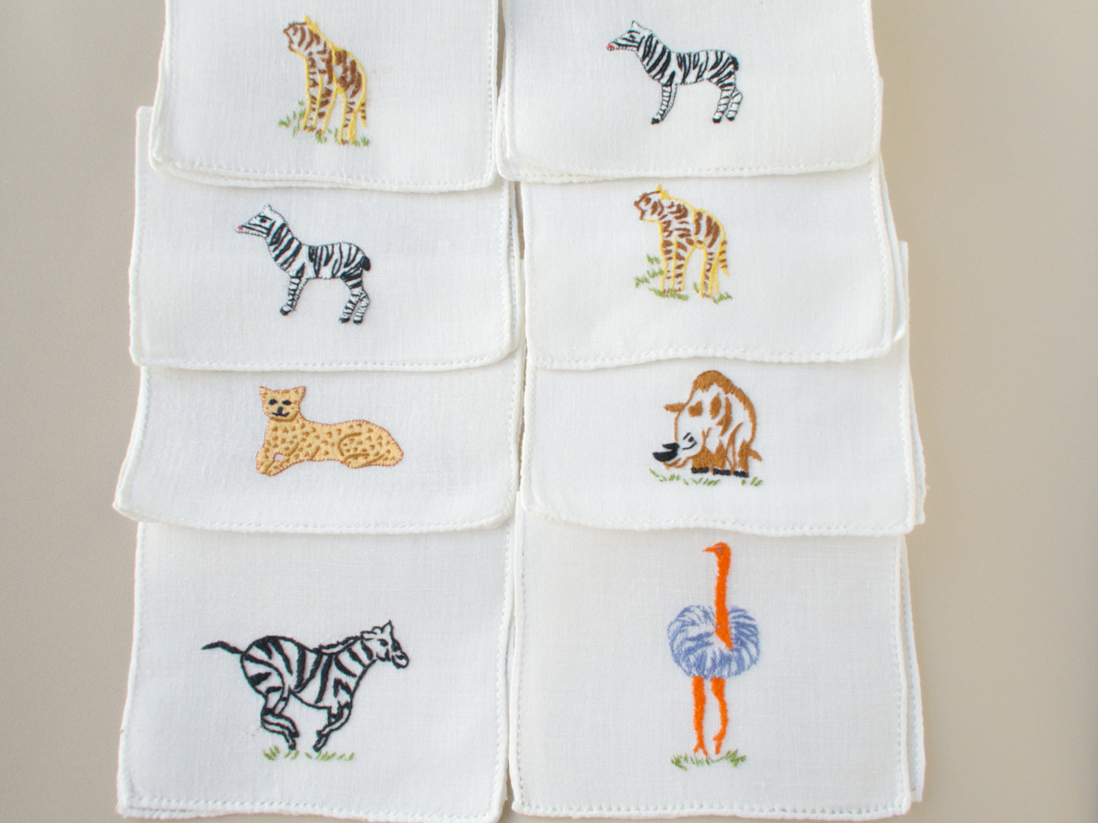 Eight vintage Italian cocktail napkins laid out showing full set of safari animal embroideries including zebra, ostrich and tiger