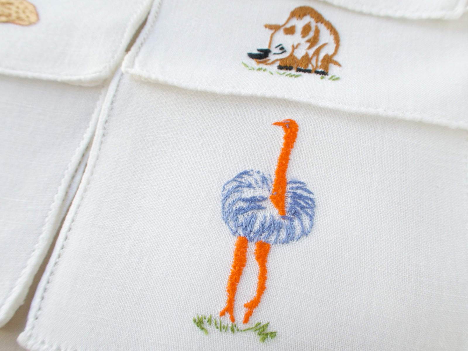 Close-up of vintage Italian cocktail napkin showing embroidered ostrich with orange legs and blue plumage