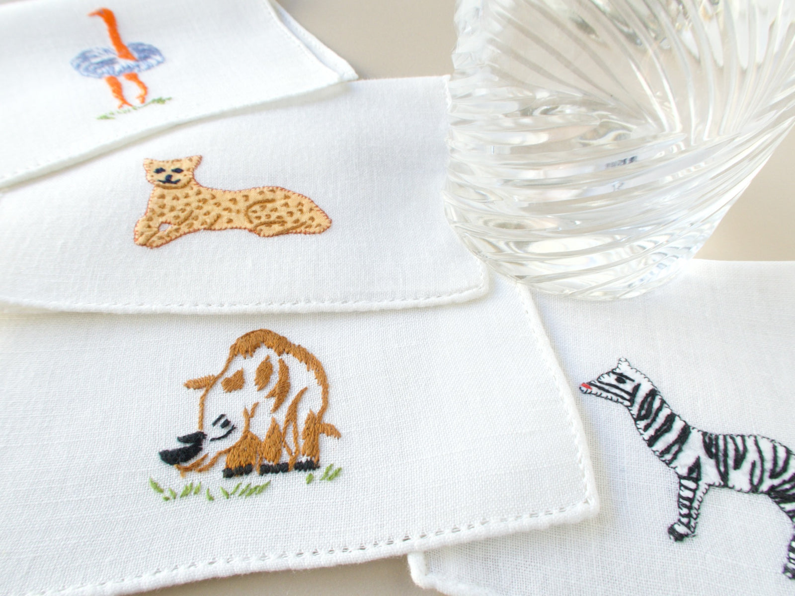 Vintage Italian cocktail napkins fanned out showing ostrich, rhino, zebra and leopard embroidery on white semi-sheer linen