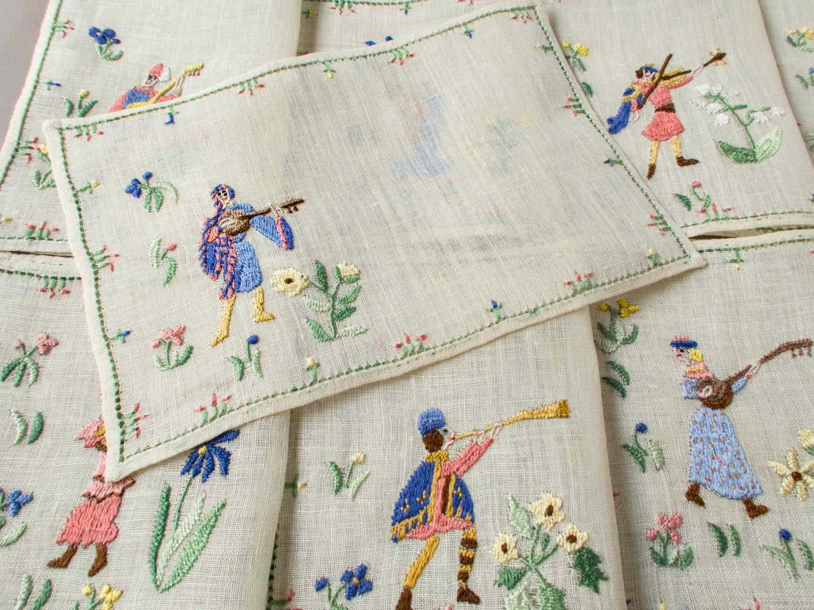 Overhead view of musician napkins, including a violinist and trumpeter, with surrounding floral embroidery.