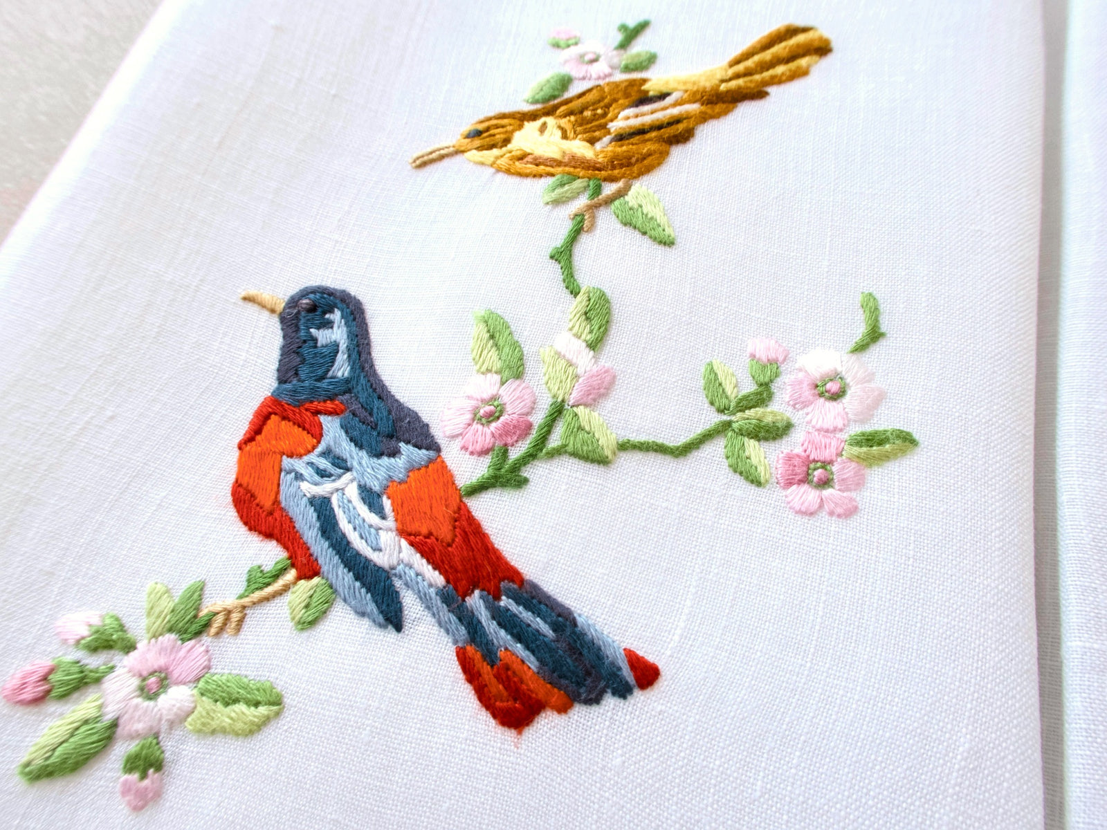 Close-up of vintage Madeira guest towel showing naturalistic songbird embroidery with wren and robin on flowering branch, fine color shading