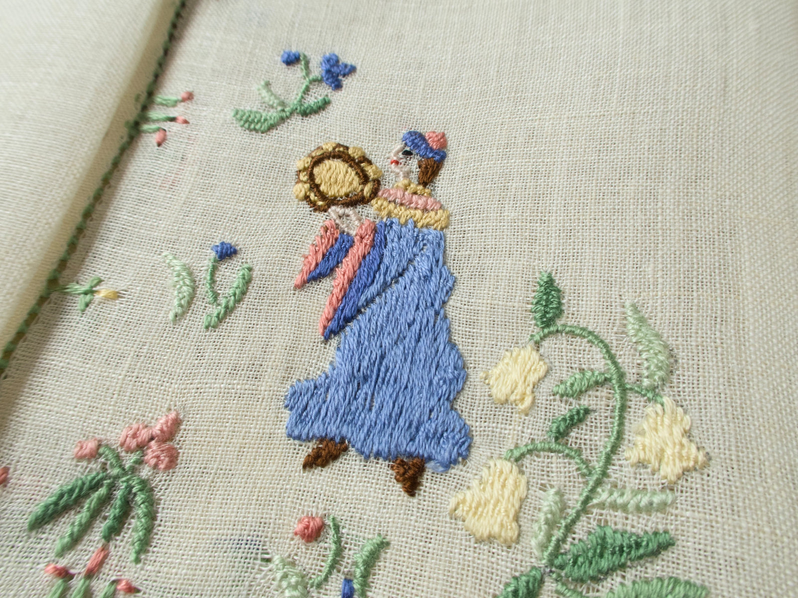 Close-up of a dancing musician with a blue dress and tambourine on embroidered linen.
