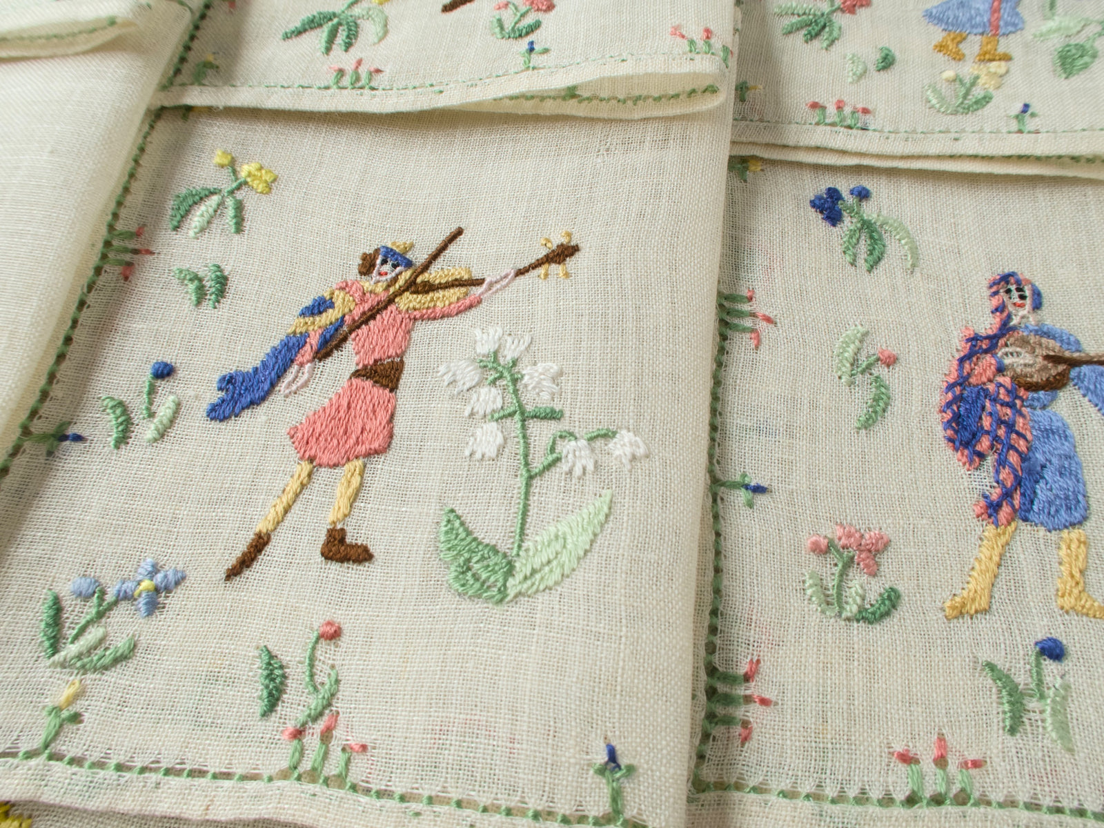 Two musician napkins side by side showing violinist figures and floral motifs.
