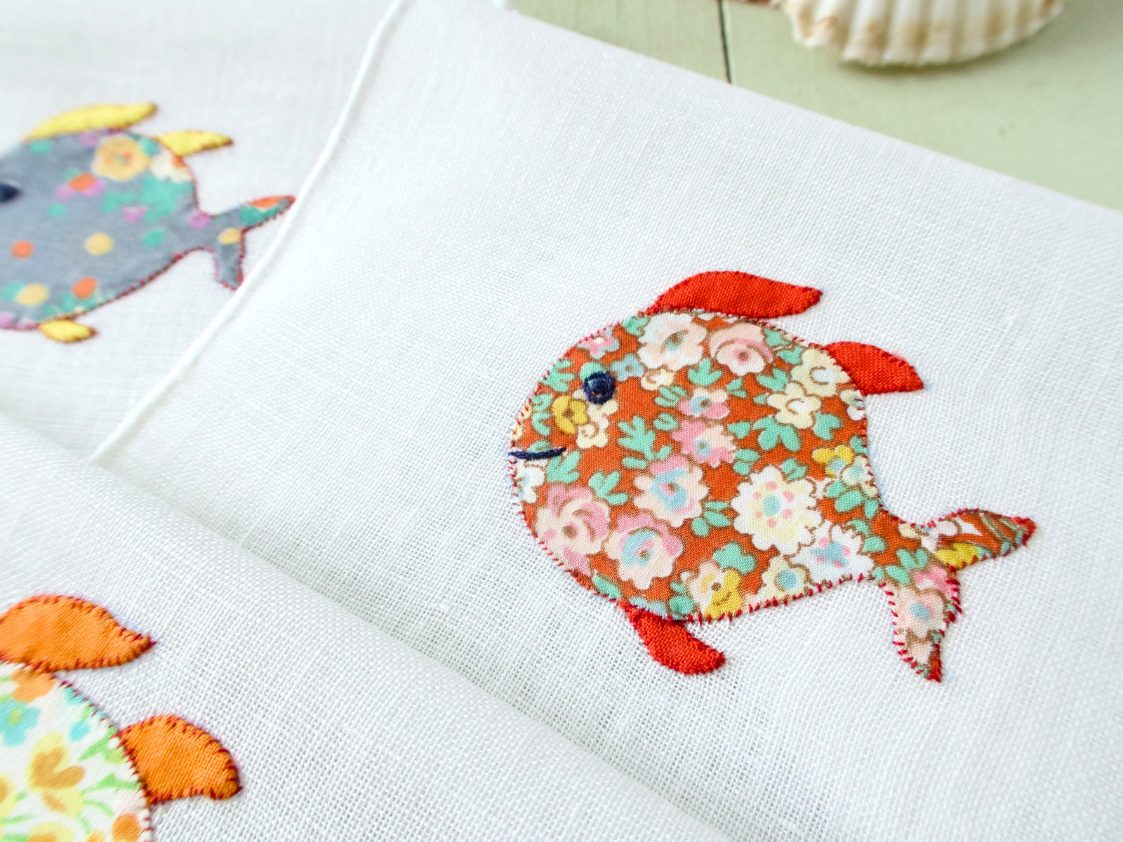 Two vintage Italian cocktail napkins showing red floral and yellow floral appliqué fish on white semi-sheer linen