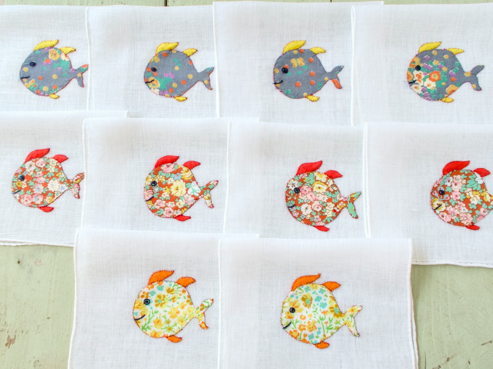 Ten vintage Italian cocktail napkins laid out in a grid showing full school of floral appliqué fish