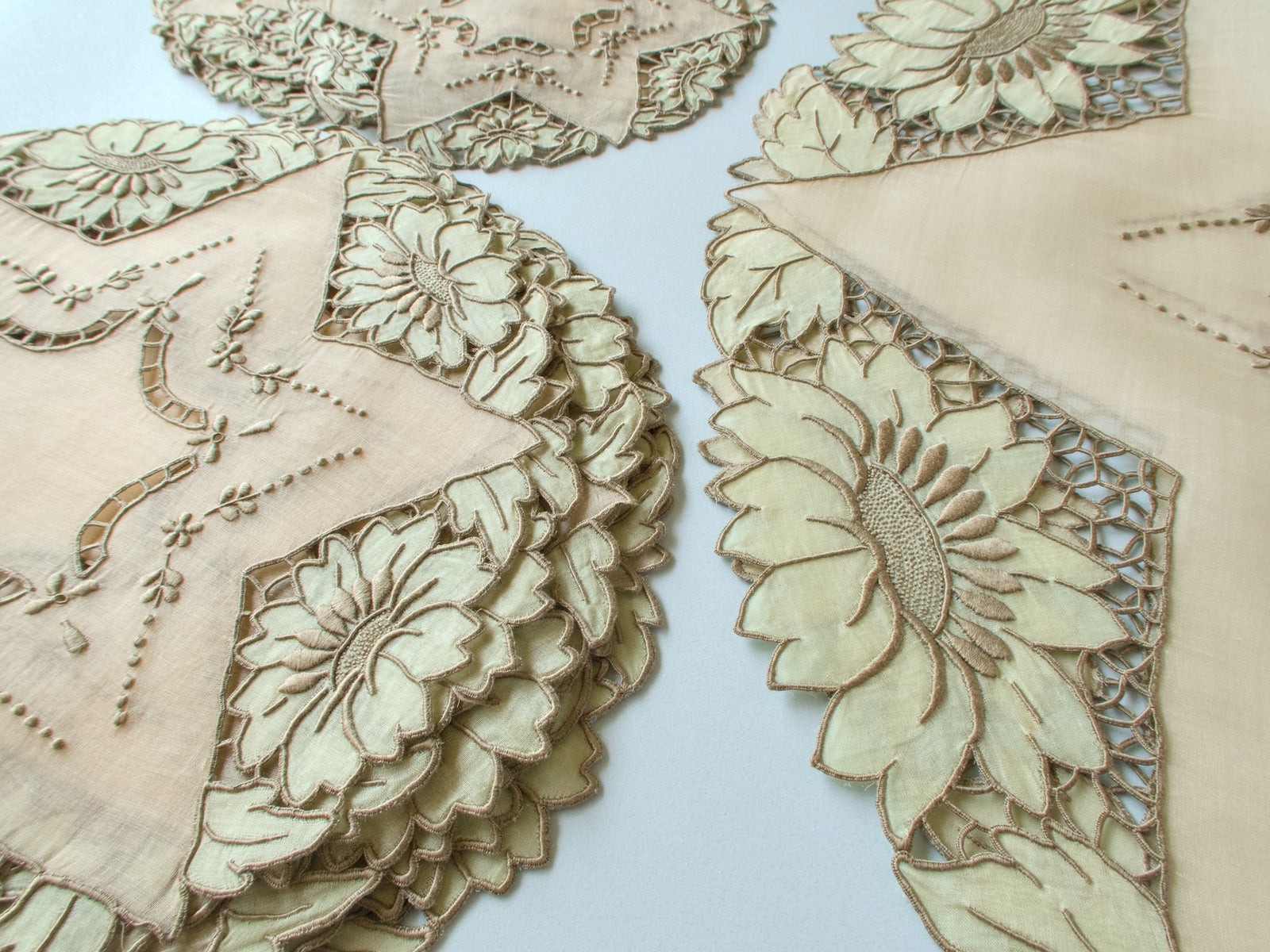 Close-up of vintage Madeira organdy placemats showing richly padded satin stitch sunflowers and appliqué in sage green with intricate Richelieu cutwork borders