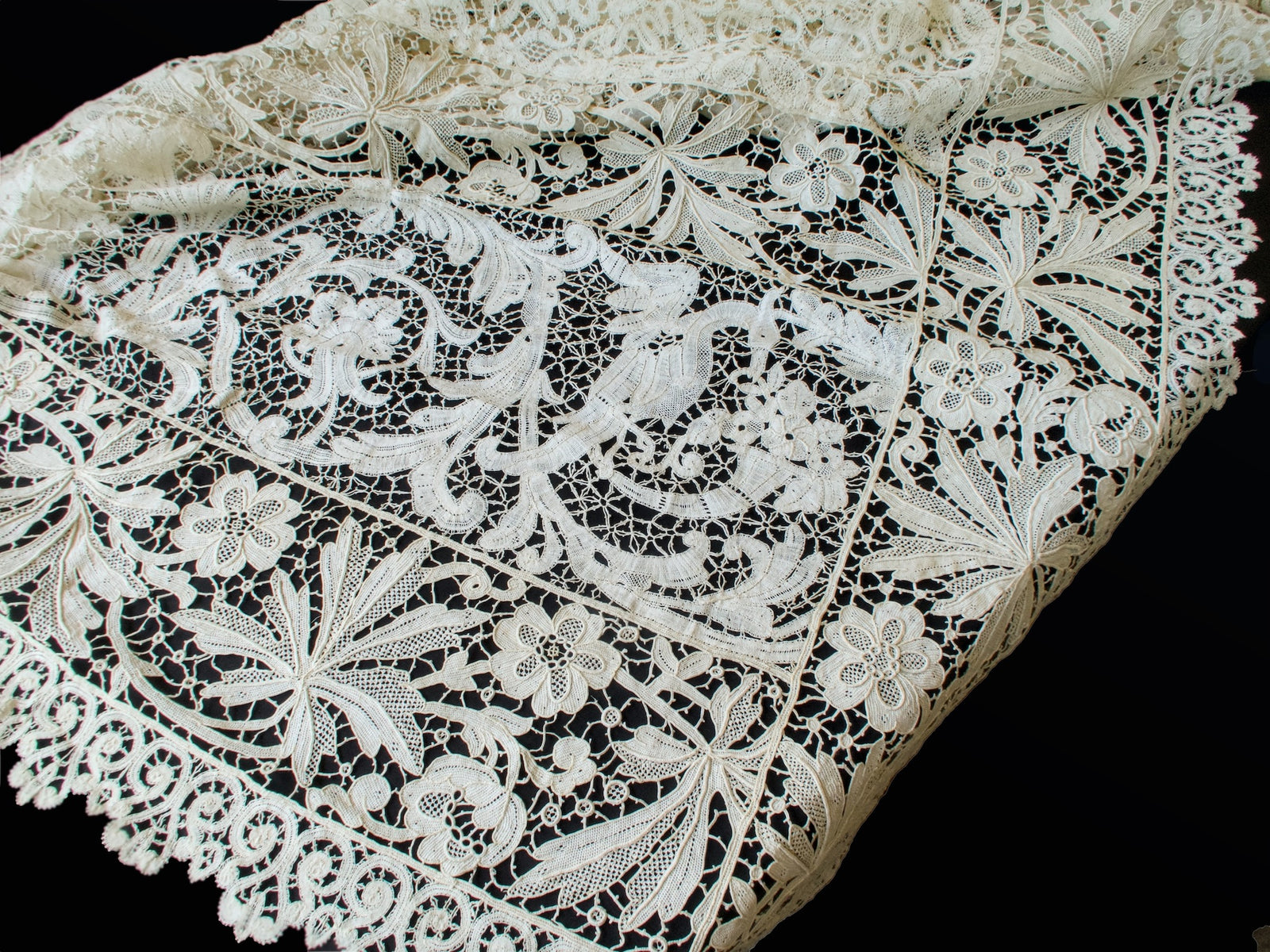 Antique French lace tablecloth corner showing a crane motif among scrolls beside floral panels and a scrolled border
