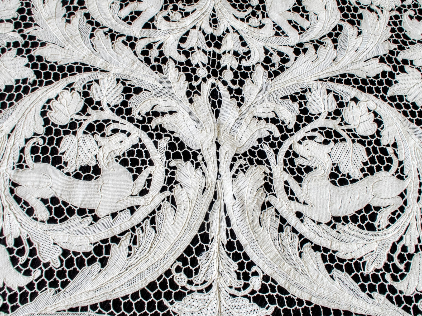 Two hounds facing each other among mirrored leaf scrolls in the lace.