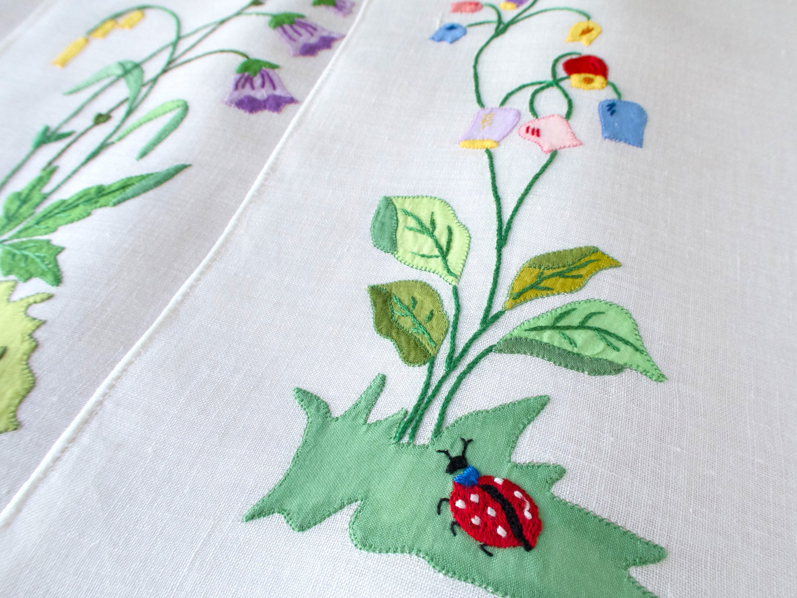 Close-up of vintage Italian linen placemat showing hand embroidered ladybug and flower detail on semi-sheer linen