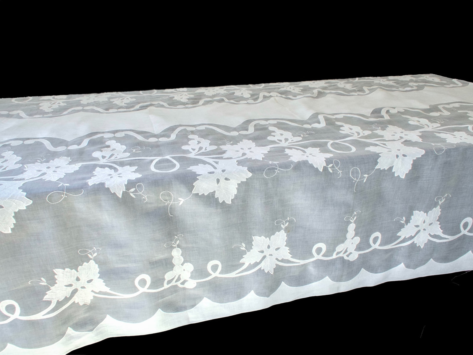 Long organdy tablecloth draped over a table, showing its sheer embroidered border and plain white center.