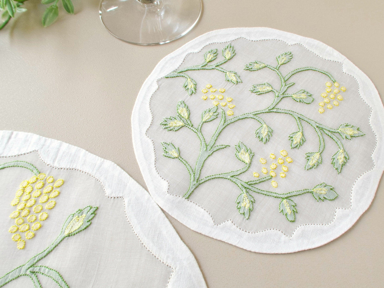 Vintage Madeira organdy coaster with Jacobean vine shadow work embroidery in sage green and yellow, wine glass for scale on beige background