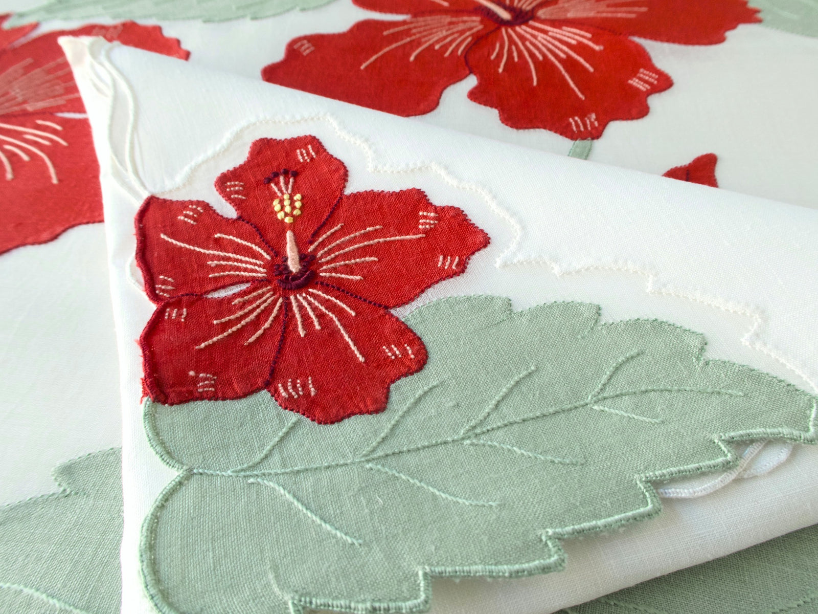 Close-up of vintage Madeira linen napkin with red hibiscus linen appliqué bloom and sage green leaf detail