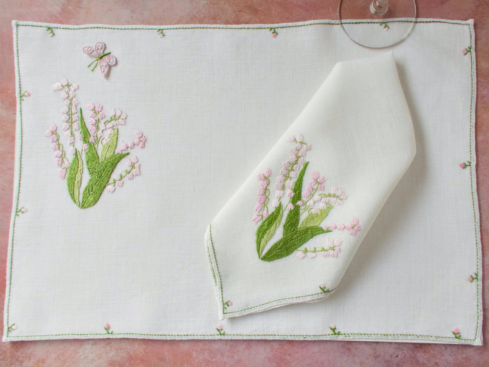 Pink Baroness Rapisardi placemat and matching napkin with lily of the valley embroidery and trembler butterfly, worked in raised punto stuoia stitch on semi-sheer Italian linen.