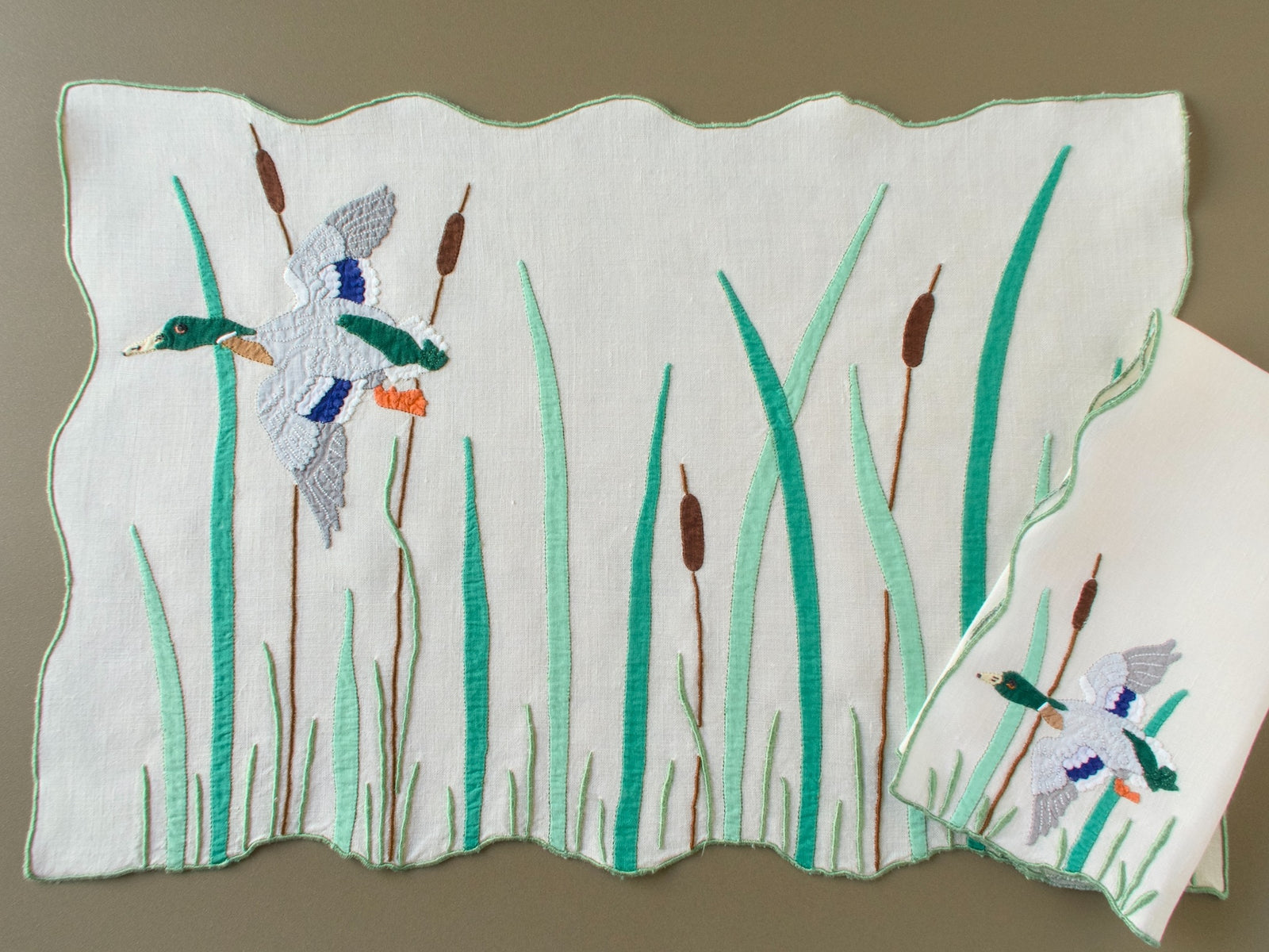 Full vintage Madeira placemat with a mallard drake flying over the marsh among tall reeds and cattails, beside a napkin with the drake at one corner