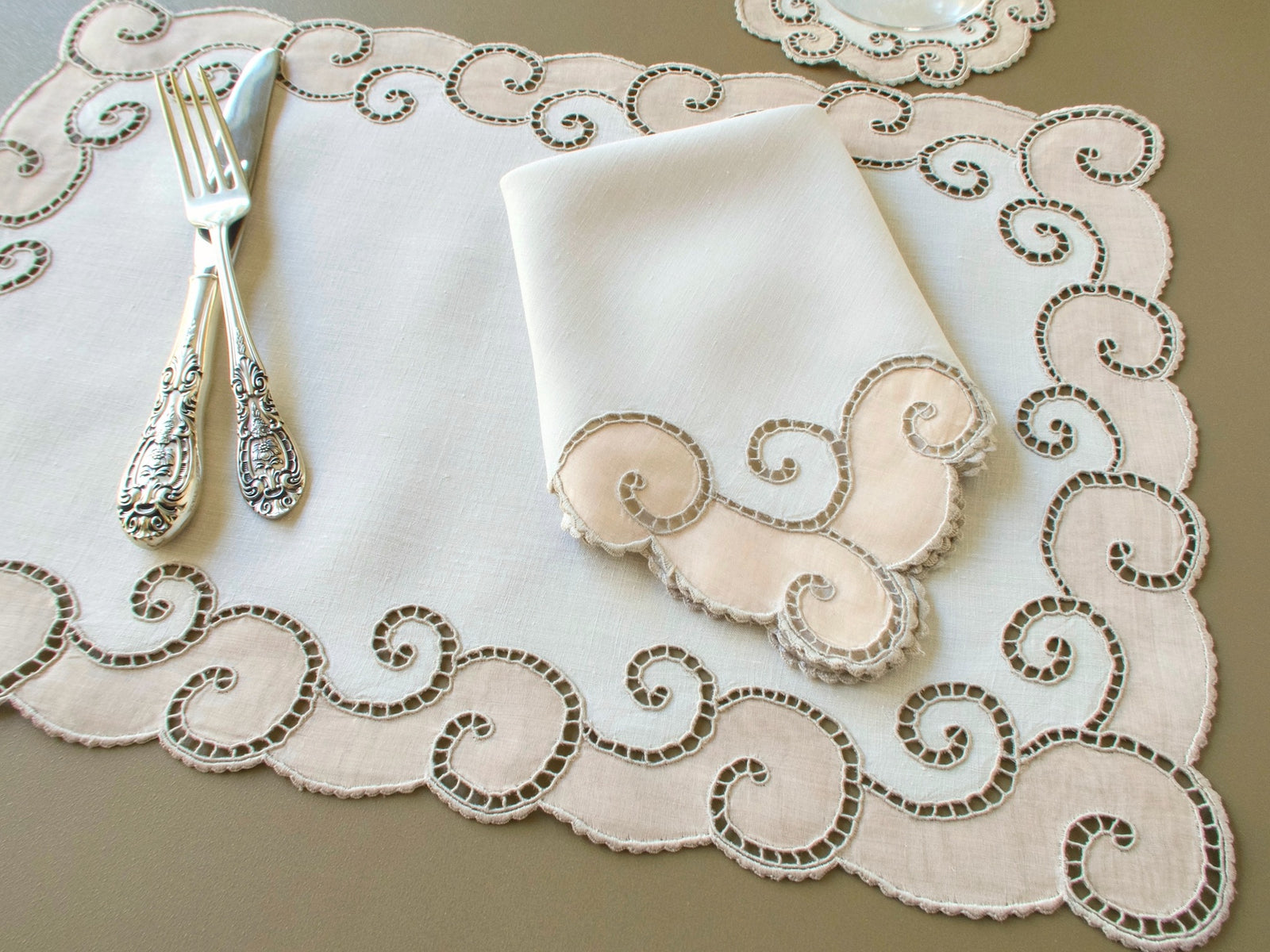 Vintage Marghab "Open Scroll" placemat with folded napkin, silver fork and knife, and a coaster at the upper edge